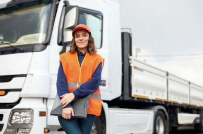 A fleet driver stands in front of her rig, smiling and preparing to drive her route.