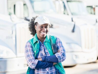 A fleet driver in front of her truck happily prepares for her day.