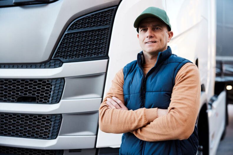 A fleet driver stands happily in front of his truck.