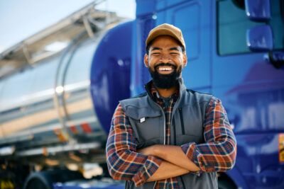 A happy fleet driver stands in front of his semi-truck.