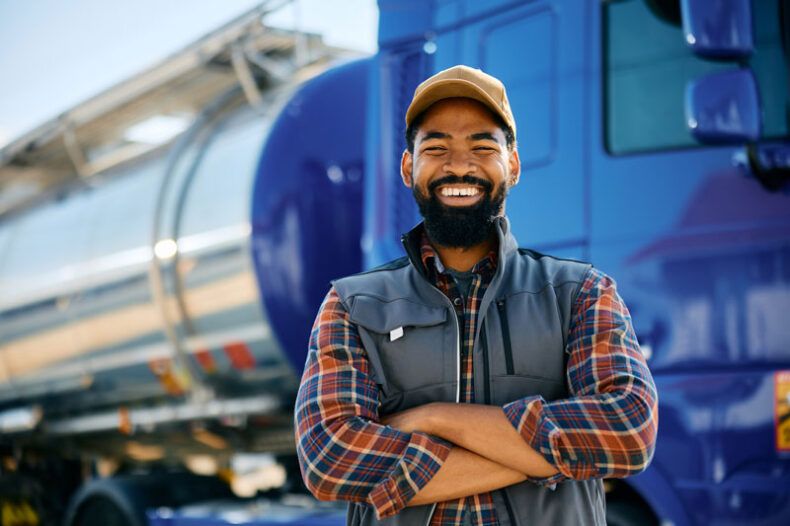 A happy fleet driver stands in front of his semi-truck.