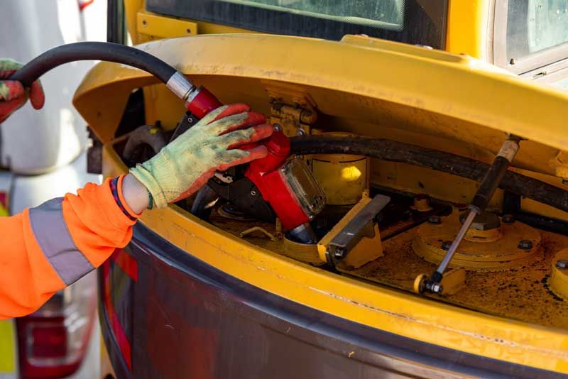 A construction worker fuels an excavator for his business.