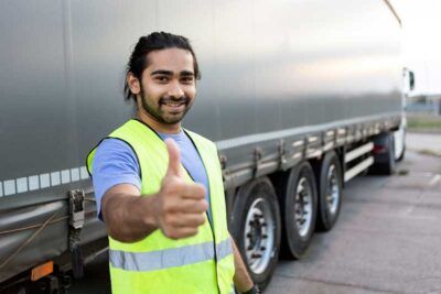 A happy truck driver gives a thumb’s up outside his rig.