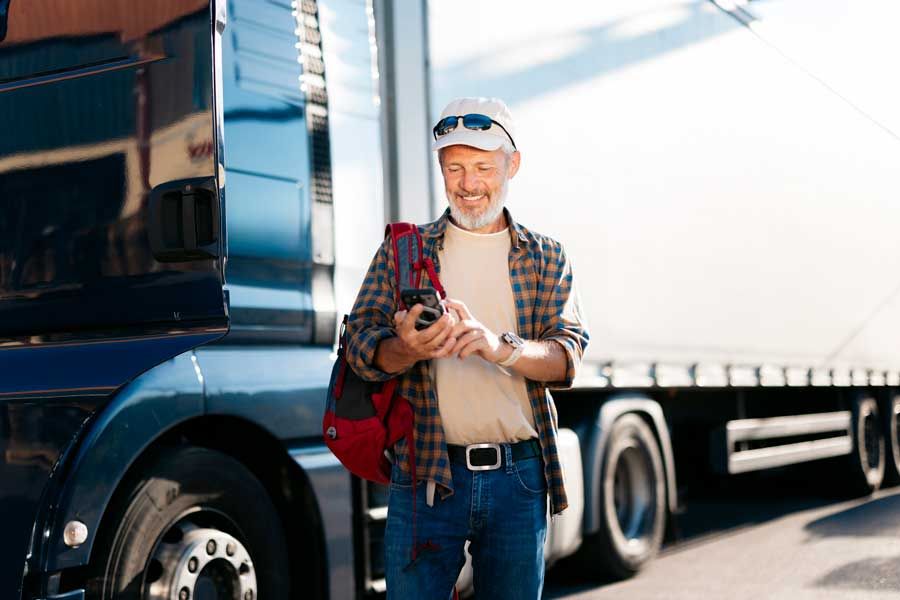A truck driver submits transaction data via his smartphone while standing outside his semi truck.